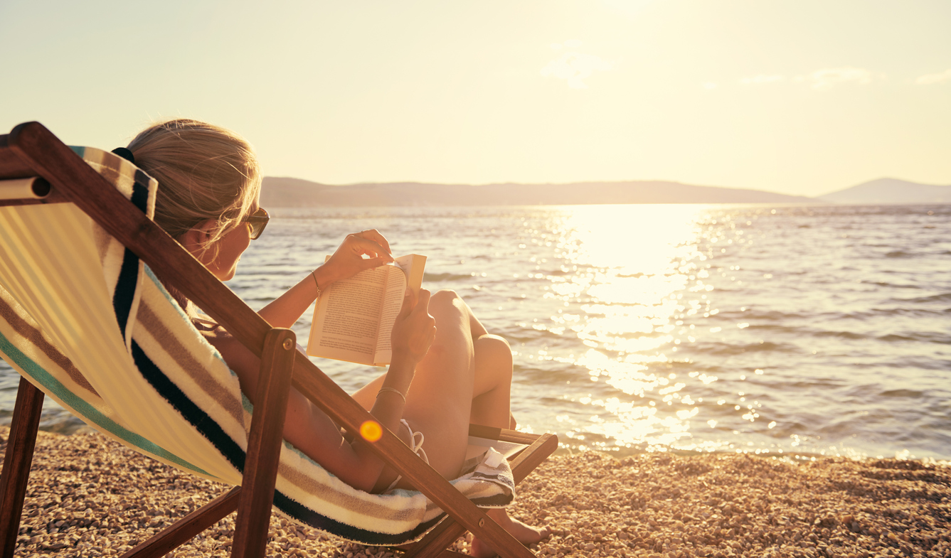 woman sitting and reading a book by the beach